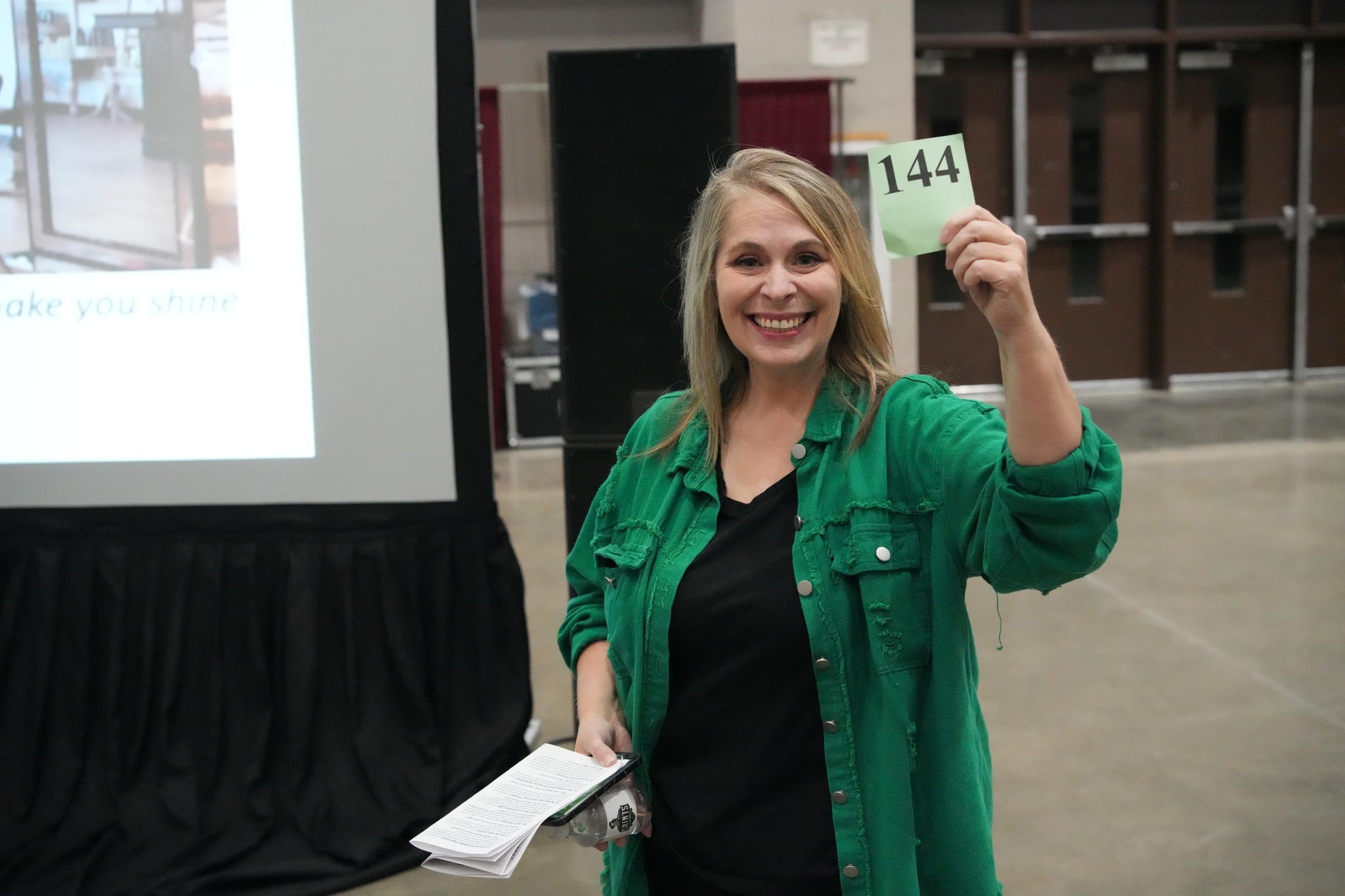Smiling woman holds up bid number during live auction event.
